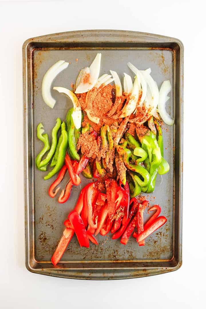 Sliced onions, green bell peppers, and red bell peppers with seasoning on a baking sheet&mdash;perfect for building flavorful Shrimp Fajita Bowls or drizzling with chipotle sauce.