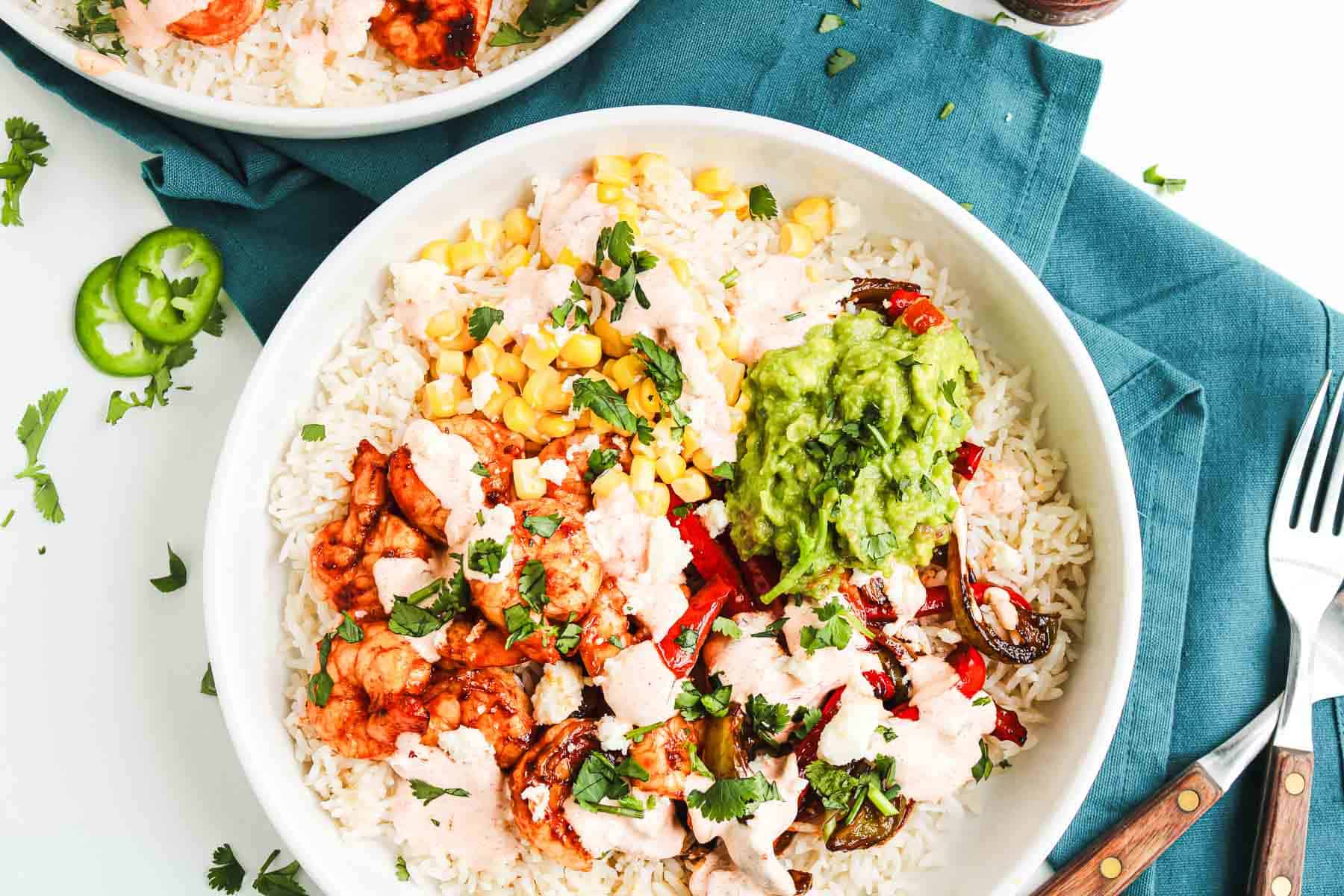 A Shrimp Fajita Bowl with rice, corn, veggies, guacamole, and chipotle sauce, all garnished with fresh cilantro.