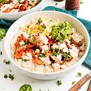 Two delicious Fajita Bowls topped with grilled chicken, veggies, guacamole, and creamy chipotle sauce, served alongside salt and pepper shakers.