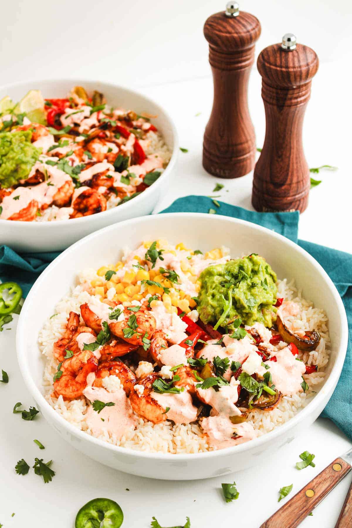 Two delicious Fajita Bowls topped with grilled chicken, veggies, guacamole, and creamy chipotle sauce, served alongside salt and pepper shakers.