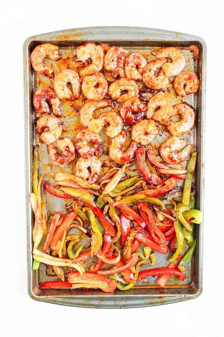 Sheet pan with cooked shrimp, sliced red and green bell peppers, and onions on a white background&mdash;perfect for assembling Shrimp Fajita Bowls. Serve with Chipotle Sauce for an extra kick of flavor.