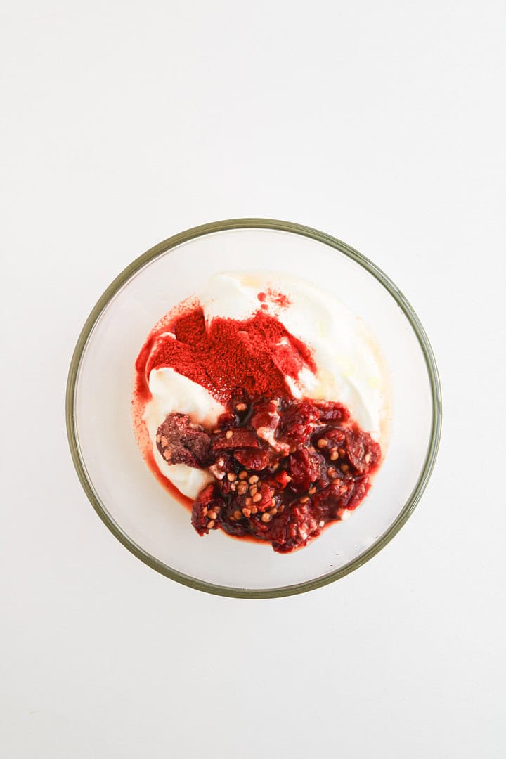 A glass bowl with yogurt, red berry sauce, a sprinkle of red powder on top, perfect as a refreshing contrast to spicy Fajita Bowls or dishes with smoky Chipotle Sauce.