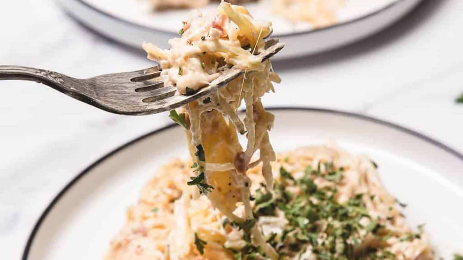 A plate of creamy spaghetti with shredded chicken, topped with chopped parsley and black pepper.