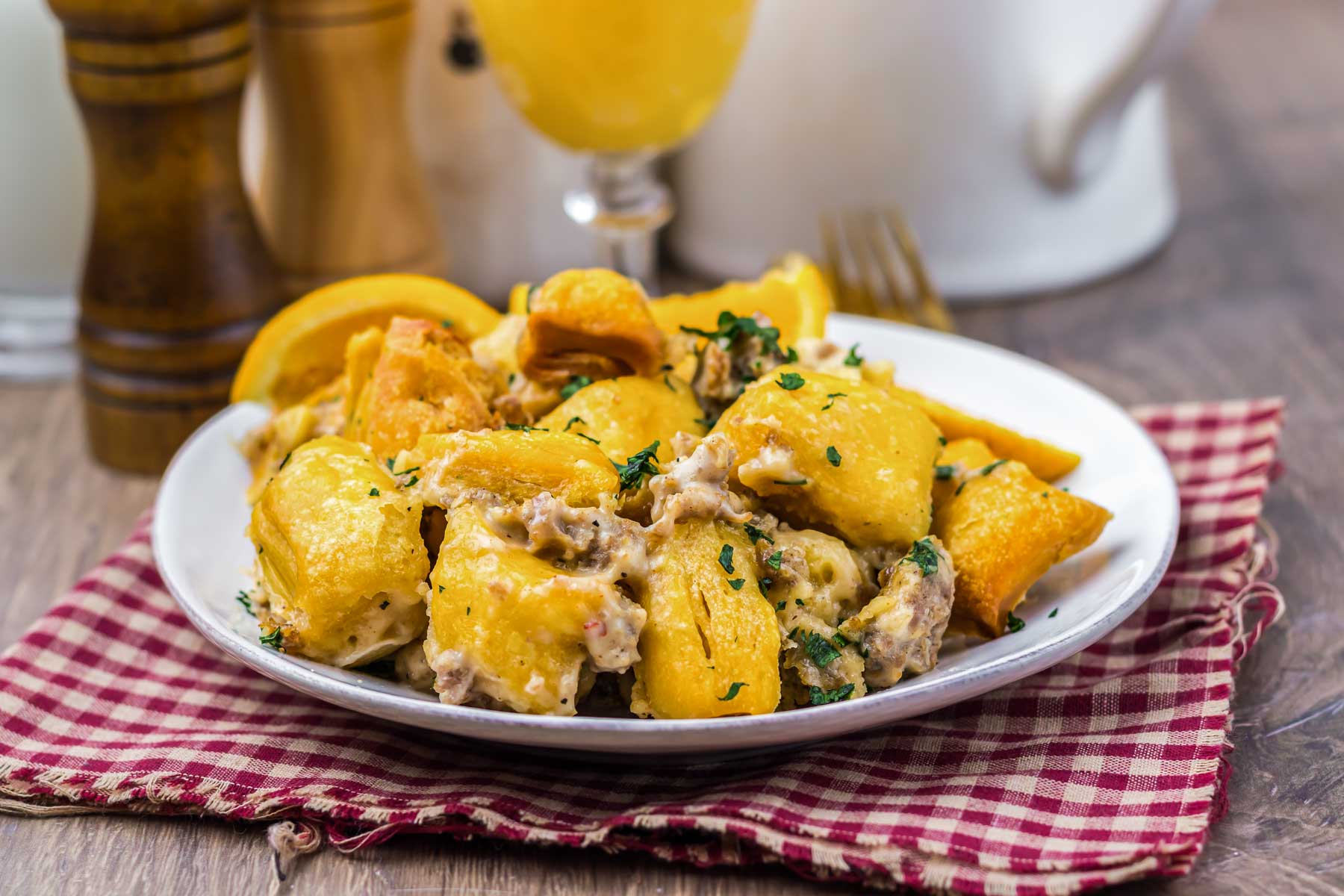 Plate of gnocchi with creamy sauce, mushrooms, and herbs on a red checkered cloth, lemon wedges on the side.