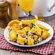 Plate of cheesy breakfast potatoes with herbs, served with orange juice on a red checkered cloth.