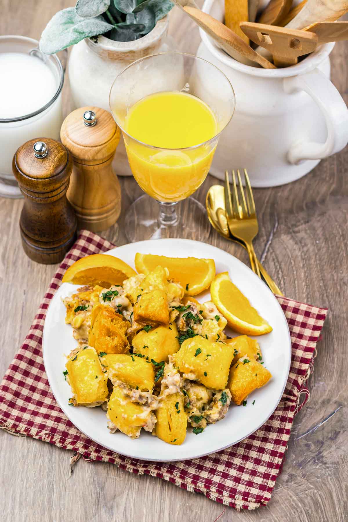 A plate of food with fried potatoes, herbs, and orange slices sits next to a glass of orange juice on the table, accompanied by a savory sausage biscuit.