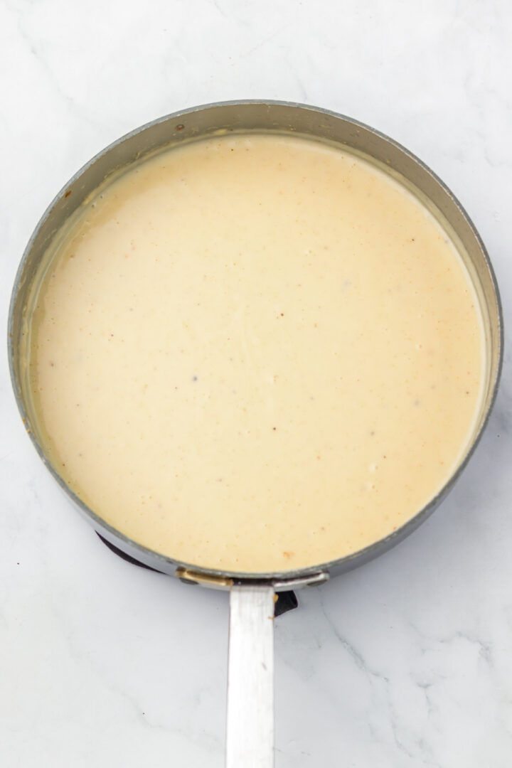 A saucepan filled with creamy, light-colored sauce on a white marble surface.