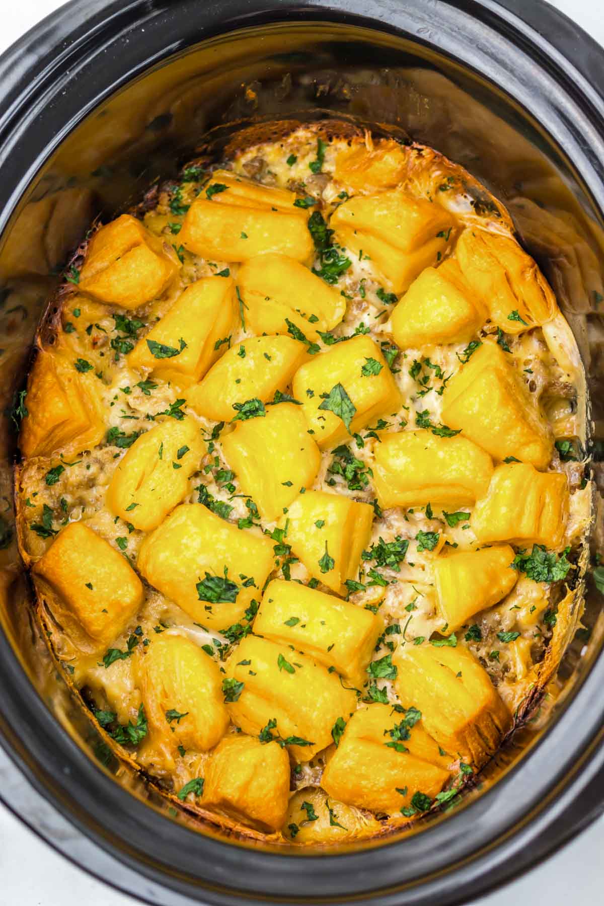 A slow cooker gravy casserole topped with golden tater tots and garnished with chopped parsley.