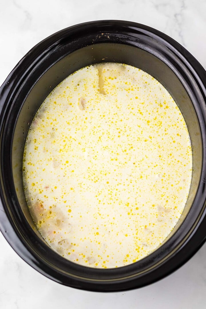 Creamy Chicken Gnocchi Soup with visible oil droplets simmering in a black Slow Cooker on a white surface.