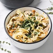 Two bowls of Chicken Noodle Soup with wide noodles, vegetables, and chopped herbs on top sit on a white surface—perfect for trying a cozy slow cooker recipe at home.