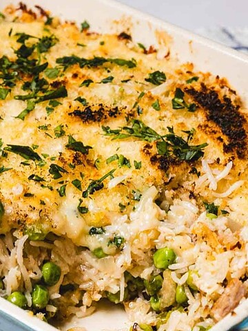 Baked casserole with golden cheese topping, rice, green peas, and herbs in a blue dish.