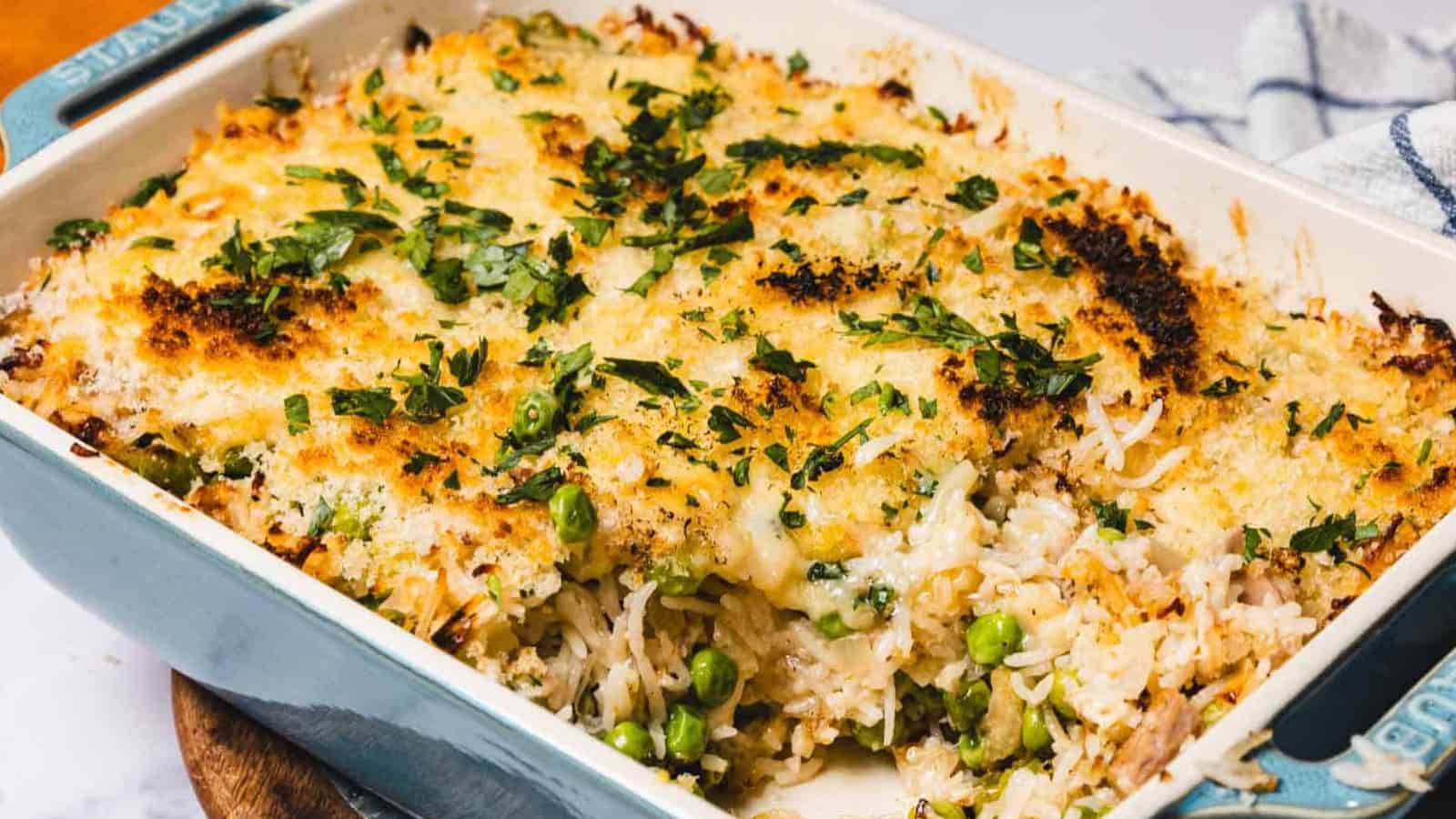 A baked casserole topped with melted cheese and herbs, with rice and green peas visible inside.