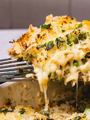 A cheesy, golden-brown casserole being lifted with a spatula, showing melted cheese and vegetables.