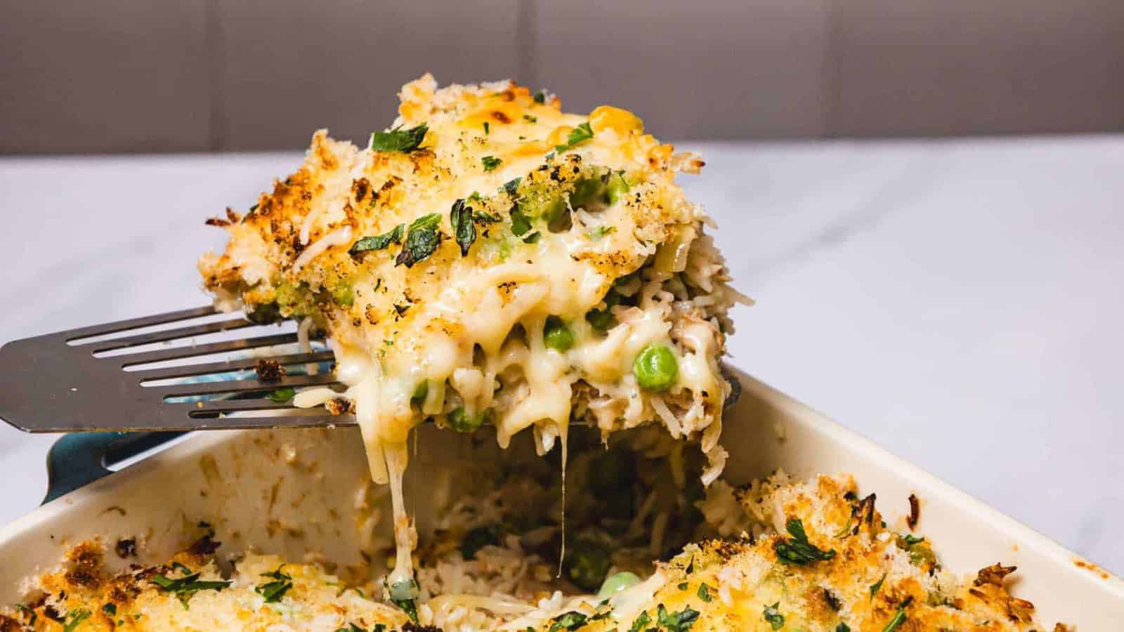 A cheesy, golden-brown casserole being lifted with a spatula, showing melted cheese and vegetables.