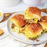 Four homemade sliders with sesame buns, lettuce, and beef patties on a plate—perfect for anyone craving tasty Big Mac sliders in bite-sized form.