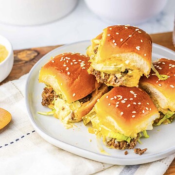 Four homemade sliders with sesame buns, lettuce, and beef patties on a plate&mdash;perfect for anyone craving tasty Big Mac sliders in bite-sized form.