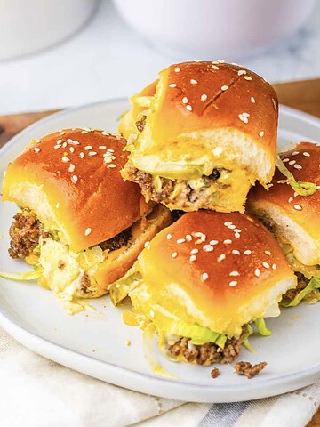 Four homemade sliders with sesame buns, lettuce, and beef patties on a plate—perfect for anyone craving tasty Big Mac sliders in bite-sized form.