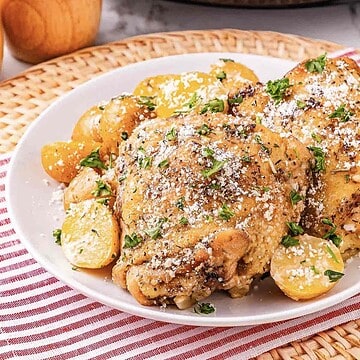 Garlic parmesan chicken thighs with roasted baby potatoes, sprinkled with herbs and grated cheese, served on a white plate.