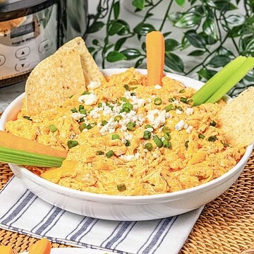 A bowl of creamy Buffalo Chicken Dip topped with green onions, served with chips, celery, and carrot sticks&mdash;perfect for any Crockpot party spread.
