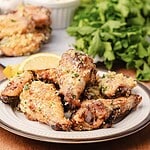 A plate of garlic parmesan chicken wings garnished with herbs and a lemon wedge, with greens in the background.