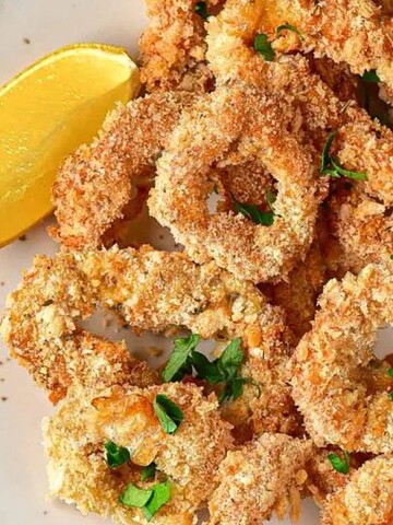 A plate of crispy breaded calamari rings garnished with parsley, served with lemon wedges.