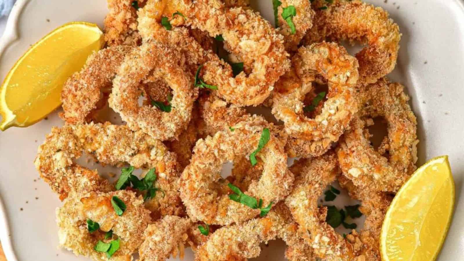 Air-fried calamari rings garnished with parsley and lemon wedges on a white plate.