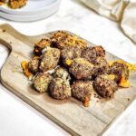 Crispy, breaded broccoli and cheese bites served on a wooden board, with sauce in a bowl and a plate in the background—perfect for making in your air fryer.