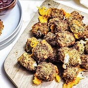 A pile of crispy, air fryer jalapeño cheese bites with melted cheese on a wooden board, next to a bowl of dip.