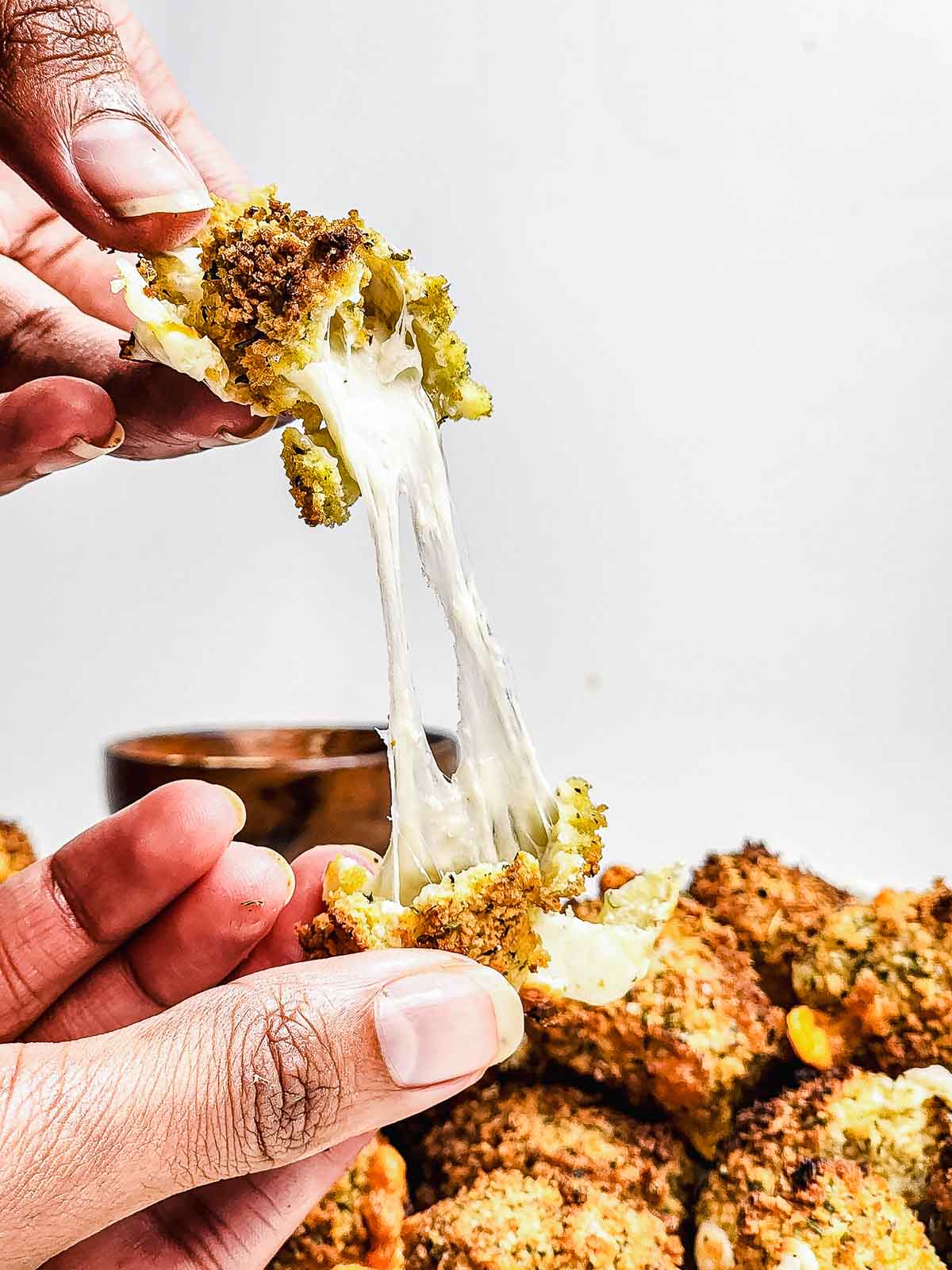 Hand pulling apart a crispy, cheesy baked broccoli bite with gooey melted cheese stretching between pieces&mdash;these irresistible cheese bites are perfect for air fryer snacking.