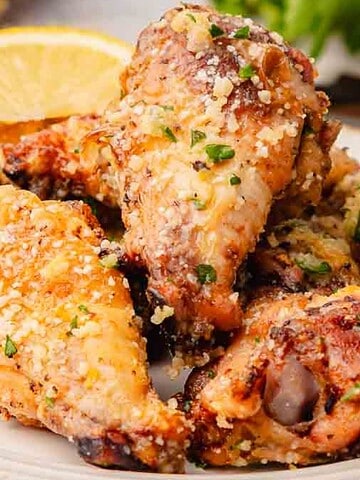 A plate of baked chicken wings garnished with herbs and grated cheese, served with a lemon wedge.