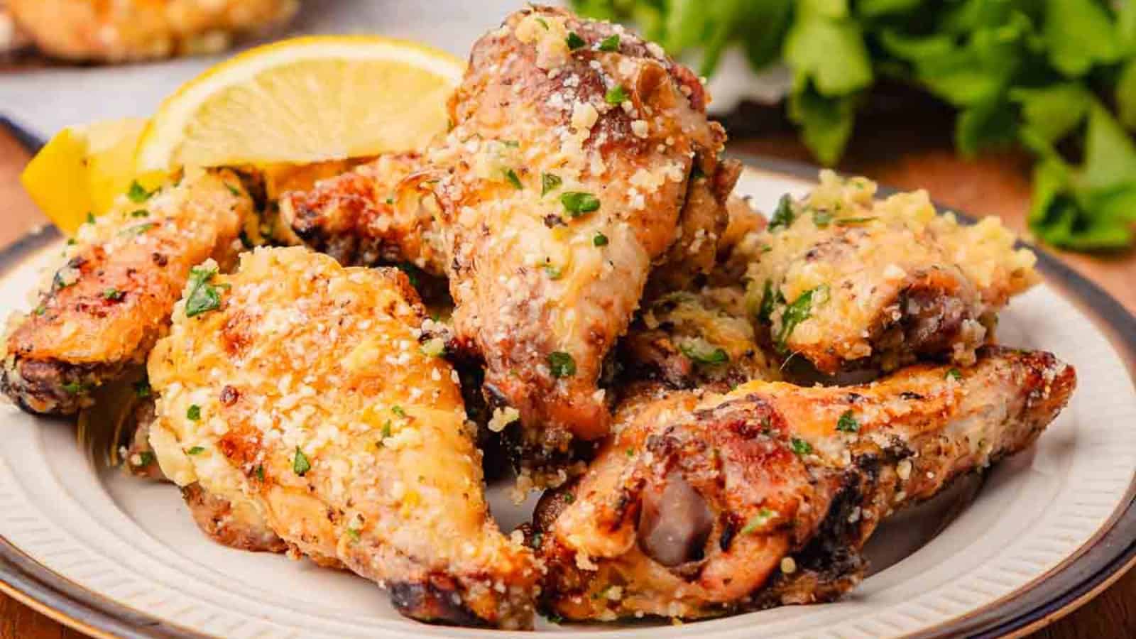 A plate of crispy garlic parmesan chicken wings garnished with herbs and served with lemon wedges.