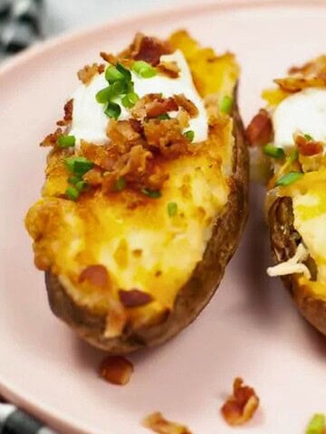 Three twice-baked potato halves topped with sour cream, bacon bits, and chopped chives on a pink plate.