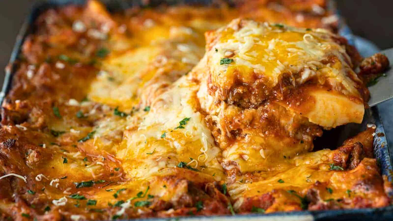 A slice of cheesy, baked lasagna being lifted from a pan, topped with herbs and melted cheese.