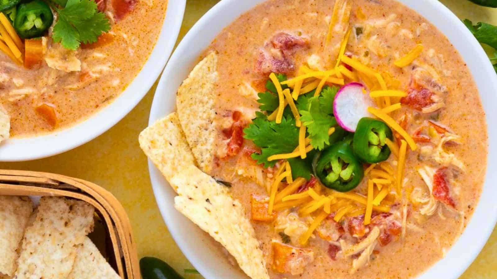 Bowl of creamy soup topped with shredded cheese, cilantro, jalape&ntilde;o, radish, and tortilla chips.
