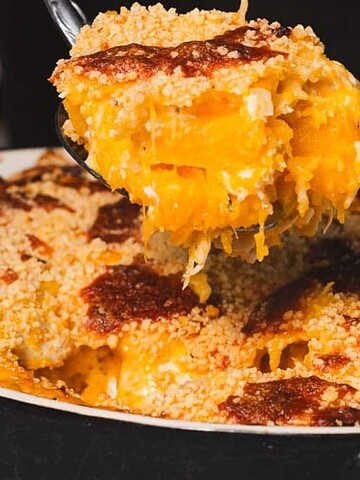 A serving of cheesy baked macaroni and cheese casserole with a golden breadcrumb topping is being lifted from a dish.