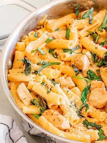 Ziti pasta with chicken, spinach, and creamy sauce in a large skillet, garnished with grated cheese.
