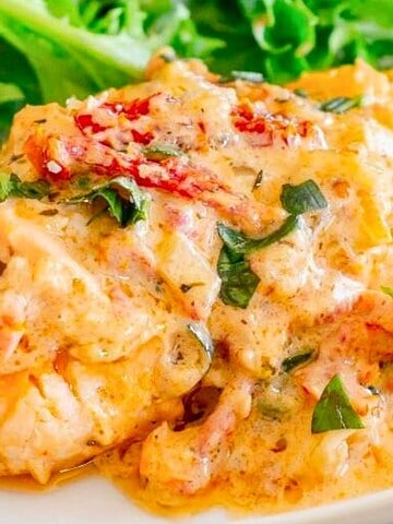 Salmon topped with creamy sauce, herbs, sundried tomatoes, with leafy greens and lemon on the side.