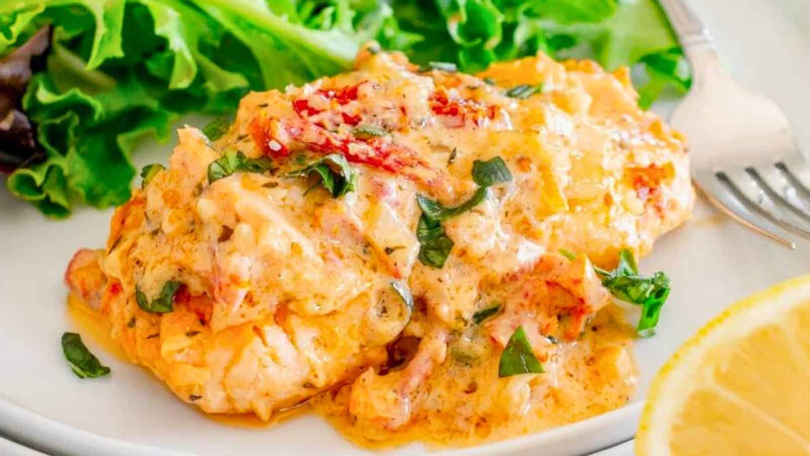 Salmon topped with creamy sauce, herbs, sundried tomatoes, with leafy greens and lemon on the side.