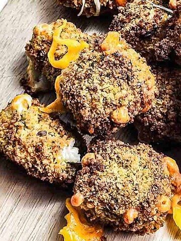 Breaded, crispy fried cauliflower bites with melted cheese on a wooden board.