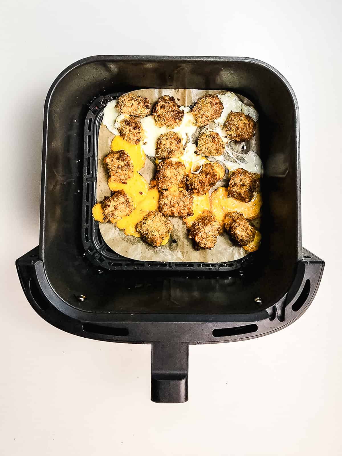 Crispy air fryer cheese bites with a golden breaded coating and melted cheese, served on parchment paper inside an air fryer basket, viewed from above.