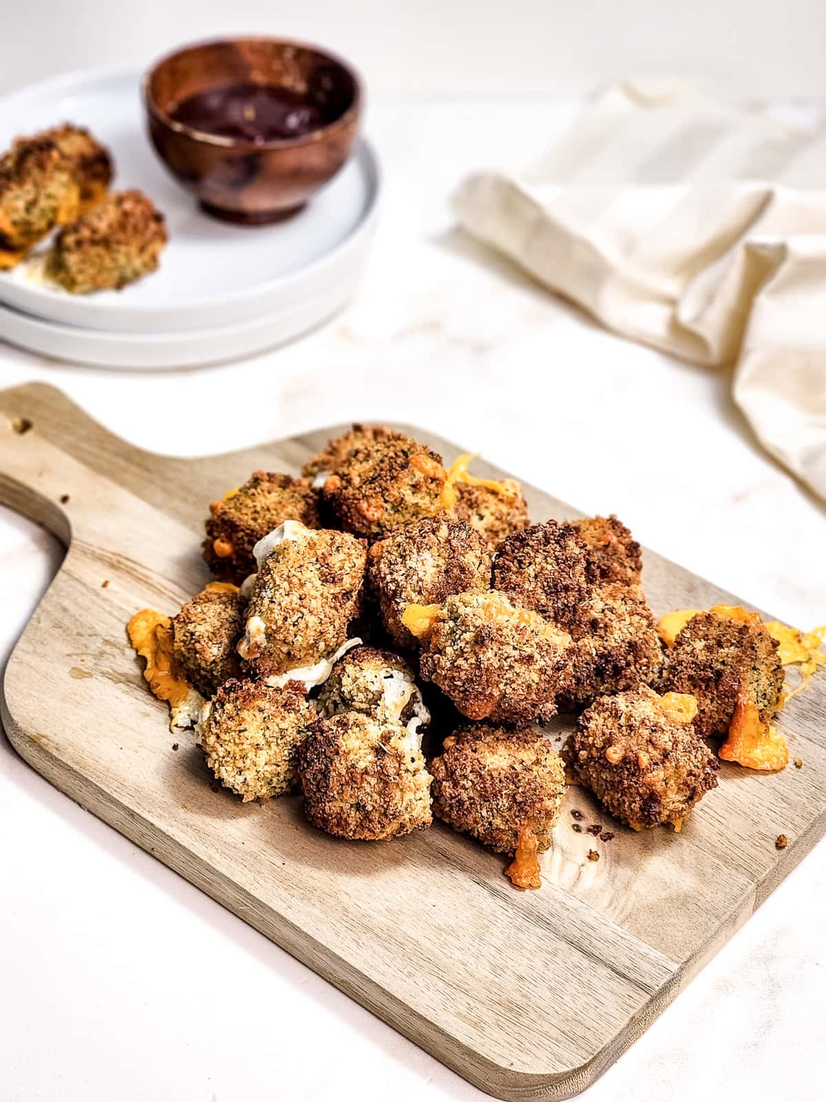 Breaded and baked cauliflower florets on a wooden board, served with dipping sauce in the background&mdash;perfect to enjoy alongside crispy air fryer cheese bites.
