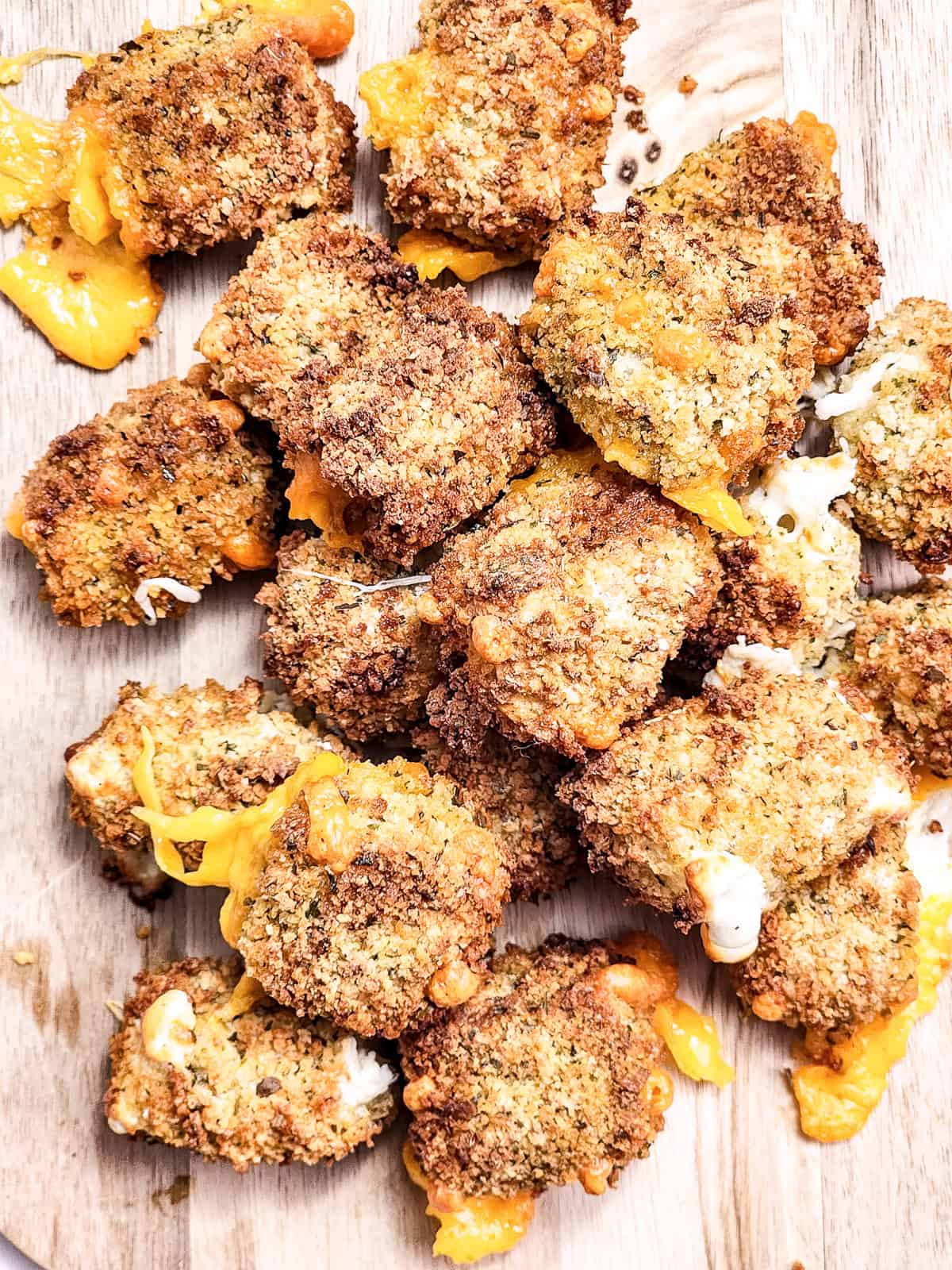 Crispy air fryer cheese bites with melted cheese oozing out, served on a wooden board.