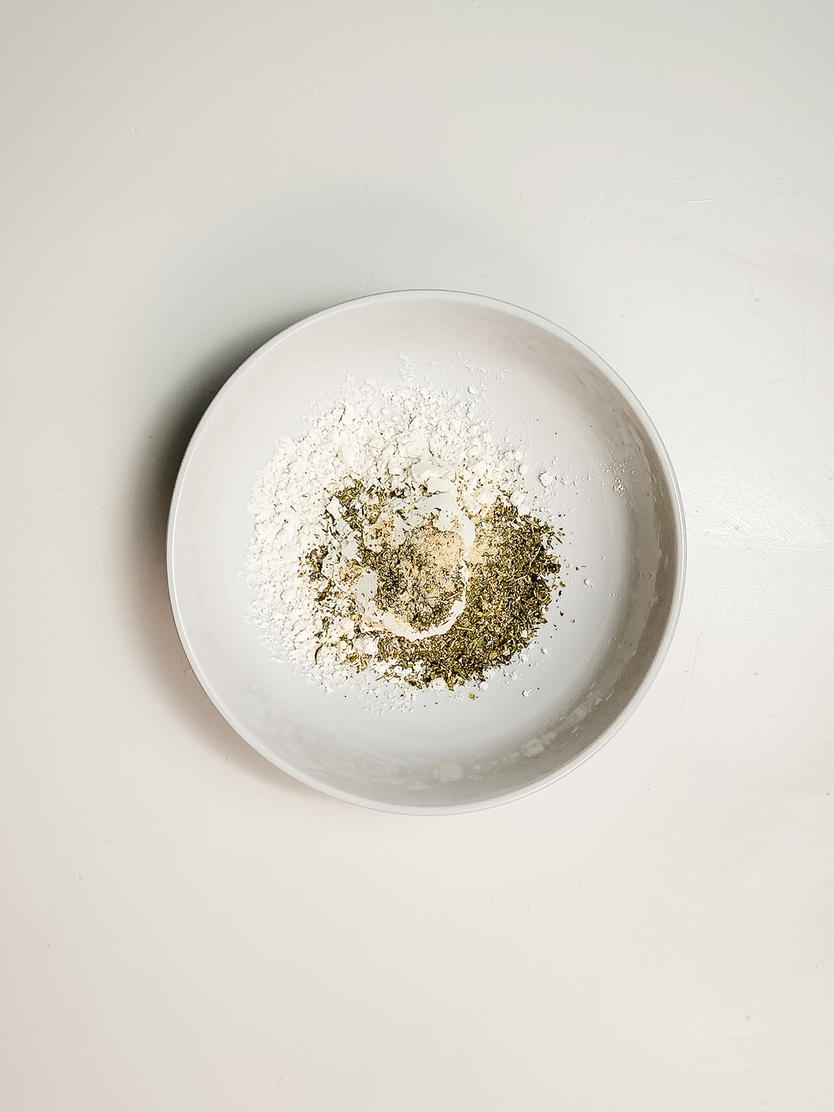White bowl with a mixture of flour and dried herbs on a plain white surface, perfect for coating crispy air fryer cheese bites.