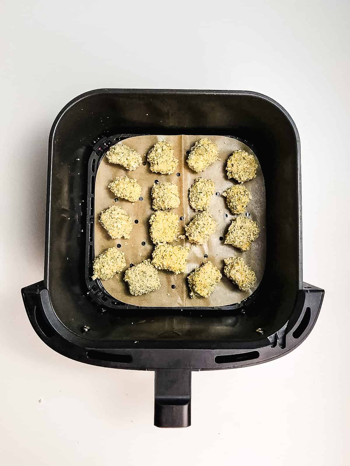 Air fryer basket with parchment paper, holding 14 crispy air fryer cheese bites arranged in rows, ready to cook.