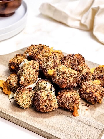 Golden brown, breaded cauliflower sits alongside crispy air fryer cheese bites with melted cheese on a wooden board.