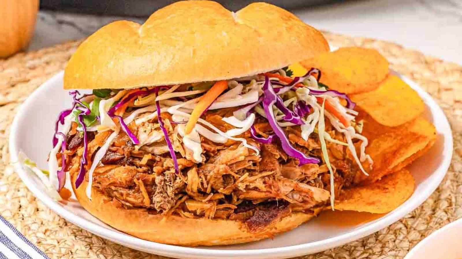 Pulled pork sandwich topped with coleslaw, served with potato chips on a white plate.