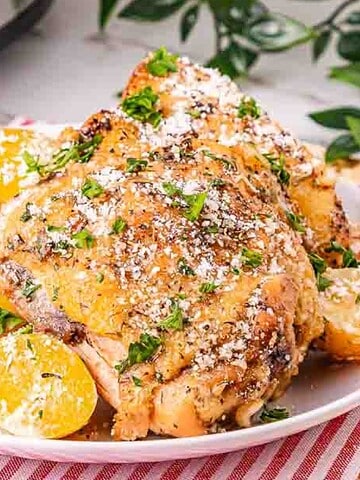 A plate of seasoned chicken and golden potatoes garnished with herbs and grated cheese on a striped napkin.