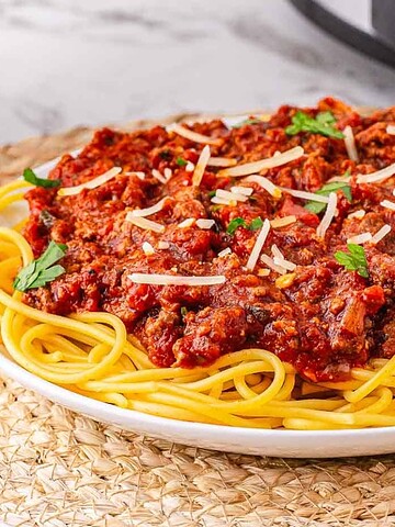 A plate of spaghetti topped with meat sauce, garnished with parsley and shredded cheese.