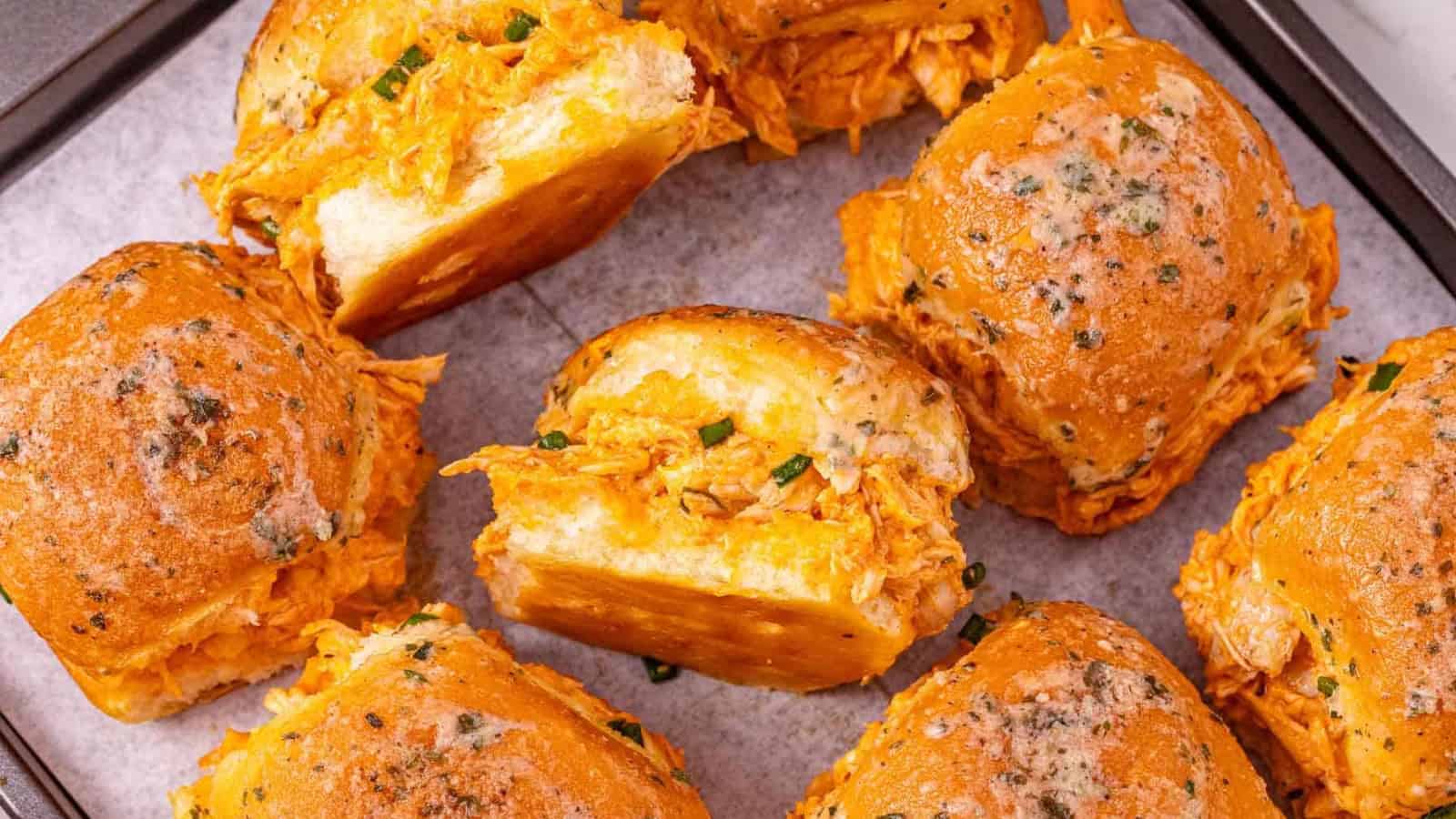 Buffalo chicken sliders with melted cheese and herbs on a baking tray, close up.