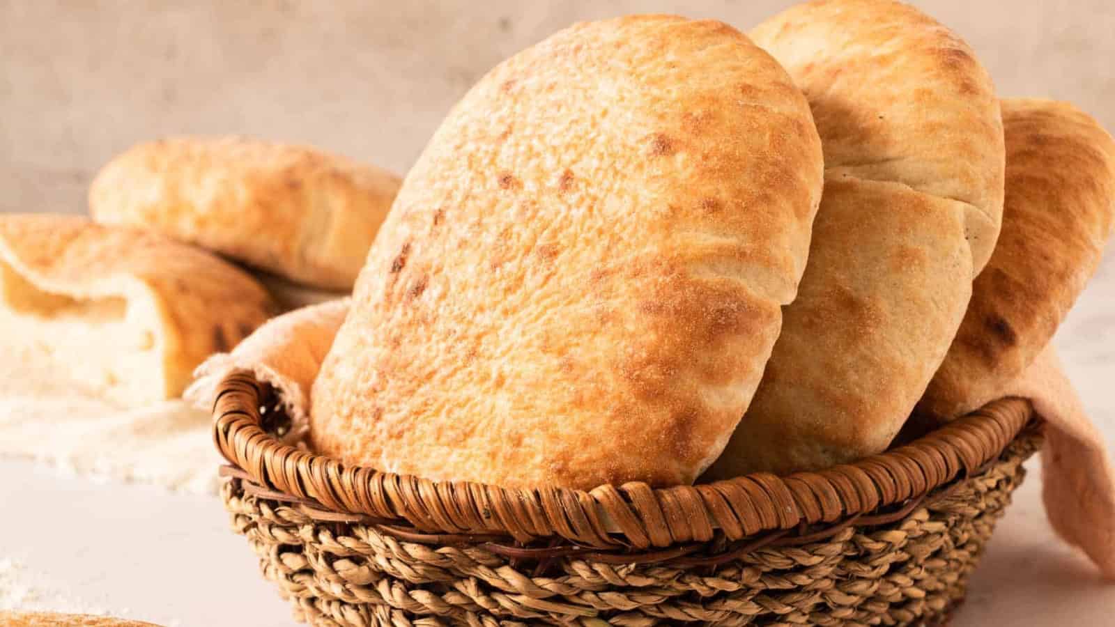A basket filled with several pieces of freshly baked pita bread on a light surface.
